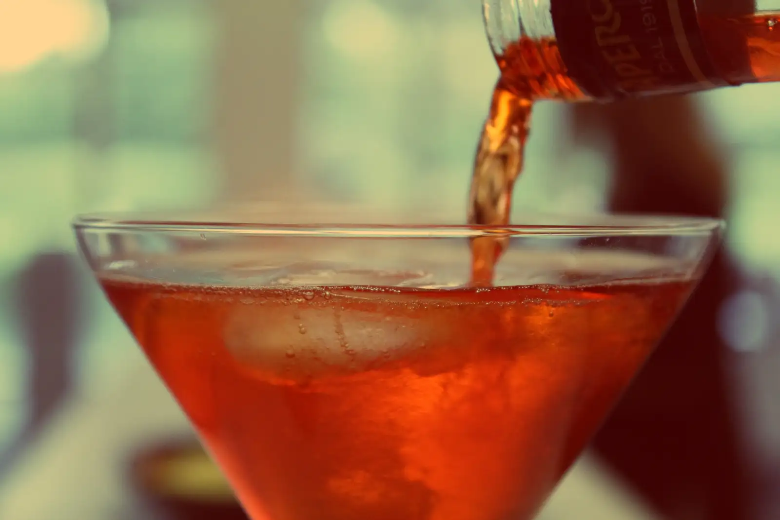 A red drink being poured from a bottle into a cocktail glass